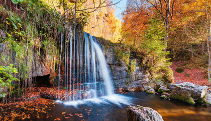 nature scene with a waterfall at autumn in the forest