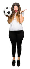 Young adult woman holding soccer football ball very happy and excited, winner expression celebrating victory screaming with big smile and raised hands
