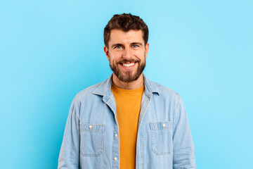 Cheerful young bearded man standing against blue studio background