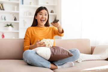 Excited young asian woman watching her favorite TV show