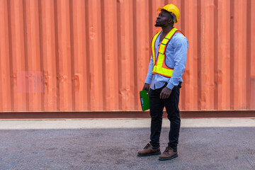 Black foreman works inspecting containers in front of the container yard to ensure timely delivery of goods.