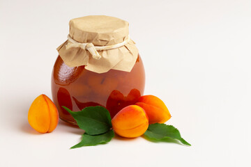 Apricot jam in a glass jar with ripe bright apricots on a white background