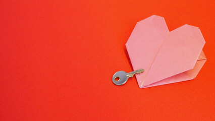 Key to your heart: a key partially placed on the left side of a pink origami heart, with orange...