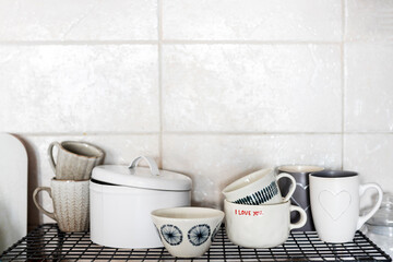 Gray and white cups with hearts and the inscription - I love you on a shelf in the kitchen against the background of a gray tiled wall.