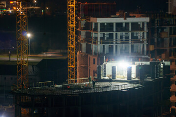 Construction site at night. Cranes working at night over an unfinished house in the light of lanterns. The concept of buying a home on credit, mortgage housing.