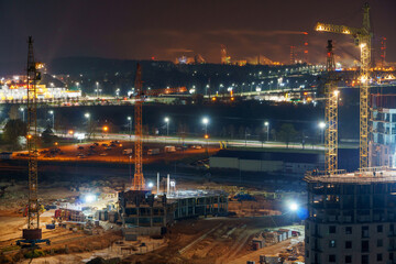 Fototapeta premium Construction site at night. Cranes working at night over an unfinished house in the light of lanterns. The concept of buying a home on credit, mortgage housing.