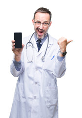 Middle age senior hoary doctor man showing smartphone screen over isolated background pointing and showing with thumb up to the side with happy face smiling