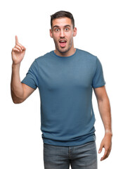 Naklejka premium Handsome young casual man pointing finger up with successful idea. Exited and happy. Number one.