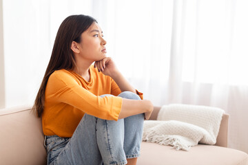 Frustrated young asian woman sitting on sofa at home
