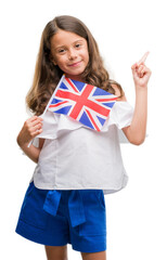 Brunette hispanic girl holding flag of United Kingdom very happy pointing with hand and finger to the side