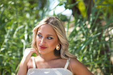 Portrait of beautiful young blonde woman posing for photos while enjoying her holiday. Tourist woman in bright beige skirt and top. In the background green vegetation. Lifestyle and travel concept.