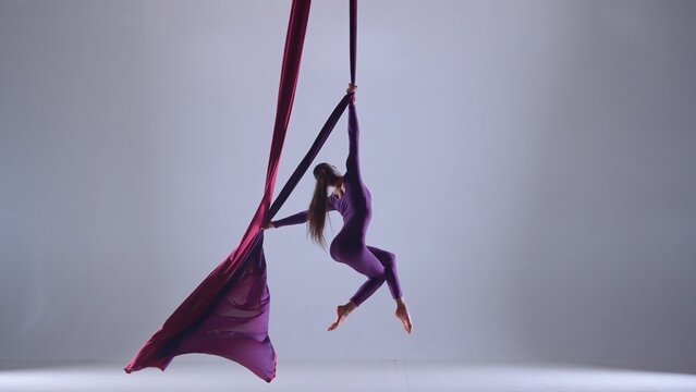Female artist isolated on blue neon studio background. Girl aerial dancer performing floating element on air silk.
