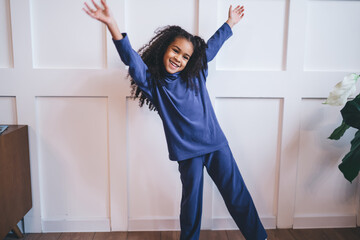 Joyful African-American young girl dancing and smiling in a bright room, her arms raised in...