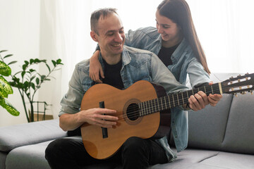 Father guy teaching girl teenager daughter guitar playing at home. Family musical lessons with strings instrument - obrazy, fototapety, plakaty
