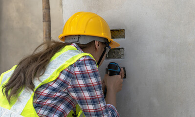 Female electrician woman drilling electric outlet on wall  in construction site