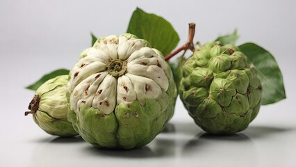 Close-up view of rare green and white cherimoya fruits with fresh leaves on a light background