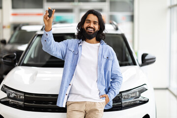 Emotional handsome eastern guy raising hand with car key