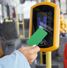 Crop of female hand holding green paying card in front of validator while boarding in public vehicle. Close up view of hand using terminal in transport. Concept of modern electronics devices.