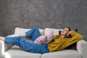 young woman is resting on the couch lying down, with a pillow in her hand