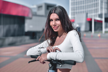 Intense gaze. Street portrait of a captivating young woman, looking directly into the camera, during a ride through the city on an electric scooter on a sunny day