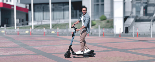 Summer adventure. An effortlessly stylish, slim young adult man joyfully rides an electric scooter...