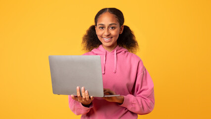 Happy teenager girl holds laptop computer smiling to camera, studio