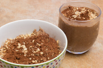 A close-up of a glass and a bowl filled with a chocolate mousse enriched with cocoa and almonds on a countertop. Quick and easy Desserts.