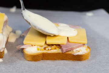 Preparing process of Croque monsieur and croque madame, grilled sandwiches with sliced ham, melted cheese, dijon mustard and poached egg on  bechamel sauce.