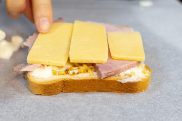 Preparing process of Croque monsieur and croque madame, grilled sandwiches with sliced ham, melted cheese, dijon mustard and poached egg on  bechamel sauce.