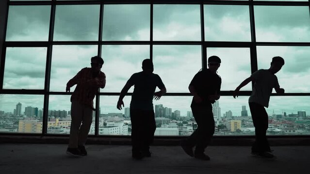 Silhouette shot of skilled choreographer group dancing together with sky scrapper or cityscape background. Young hipster team break dancing performance near window. Outdoor sport 2024. hiphop.