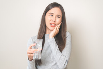 Suffering from toothache, hurt asian young woman touch cheek, face expression ache or feel pain, sensitive molar teeth, hand holding glass of water with ice, inflammation when drink cold, healthcare.
