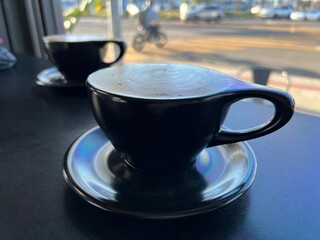 Low angle, close view across two coffee cups, with out of focus cyclist passing in background