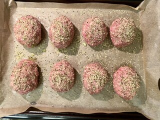 Raw Scotch eggs—soft boiled eggs wrapped in sausage meat and sprinkled with condiments—resting on parchment paper, on baking sheet, before being placed in oven to finish cooking