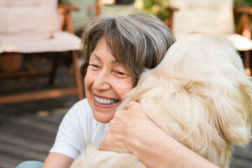 Cheerful caucasian senior old woman grandmother pet owner hugging embracing golden retriever labrador while walking outdoors in park at the porch of a house