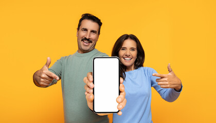 Enthusiastic couple showcasing a smartphone with a blank screen, the man