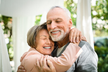 Happy senior old elderly couple spouses hugging embracing with eyes closed in garden forest outdoors. Love and care concept. Physical touch - love language
