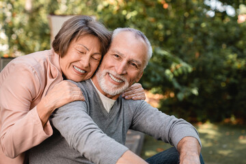 Cheerful european senior old elderly couple grandparents spouses hugging embracing bonding together in the garden forest outdoors. Love and care concept