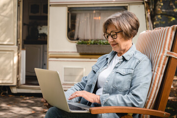 Old senior elderly businesswoman freelancer grandmother using laptop online remotely for shopping social media browsing route while traveling by trailer camper van motor home