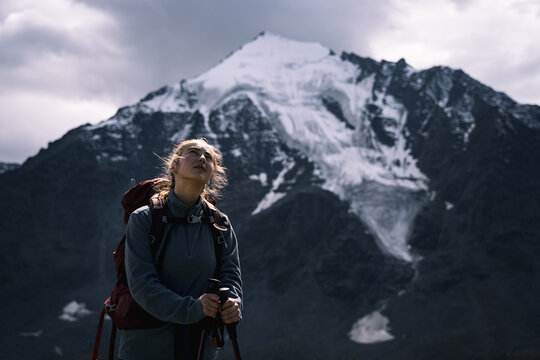 A young girl hiker against the backdrop of a snowy mountain, a tired traveler looks at the sky, a dramatic portrait of a pensive tourist