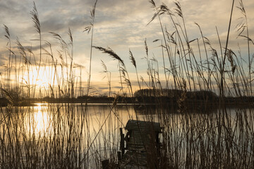 Romantic lake scene with wooden jetty and reed. at sunset in winter.