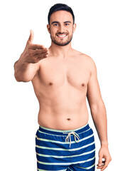 Fototapeta premium Young handsome man wearing swimwear smiling friendly offering handshake as greeting and welcoming. successful business.