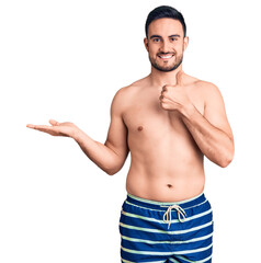 Young handsome man wearing swimwear showing palm hand and doing ok gesture with thumbs up, smiling happy and cheerful