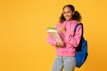 Cheerful african american student girl pointing finger aside, yellow backdrop