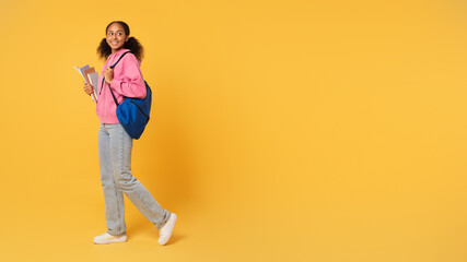 African girl student holds workbooks posing with backpack, yellow background