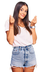 Young hispanic woman wearing casual white tshirt doing money gesture with hands, asking for salary payment, millionaire business