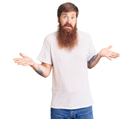 Handsome young red head man with long beard wearing casual white tshirt clueless and confused expression with arms and hands raised. doubt concept.