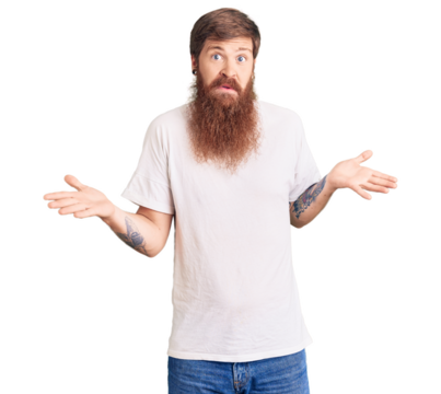 Handsome young red head man with long beard wearing casual white tshirt clueless and confused expression with arms and hands raised. doubt concept.