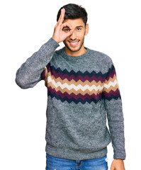 Young handsome man wearing casual winter sweater doing ok gesture with hand smiling, eye looking through fingers with happy face.