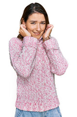 Young caucasian girl wearing wool winter sweater covering ears with fingers with annoyed expression for the noise of loud music. deaf concept.