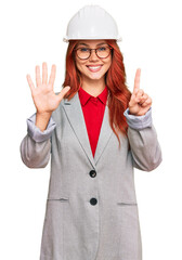 Young redhead woman wearing architect hardhat showing and pointing up with fingers number six while smiling confident and happy.